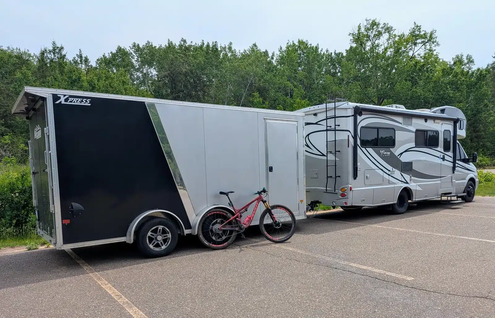Silver Winnebago View motorhome towing a 16-foot black and silver enclosed trailer, with a red mountain bike leaning against the trailer.